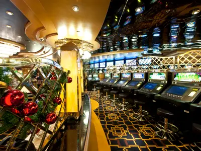 Casino der MSC Splendida, festlich mit roten Kugeln dekoriert. Beleuchtete Spielautomaten mit Hockern, goldene Akzente und spiegelnde Decke im luxuriösen Interieur.