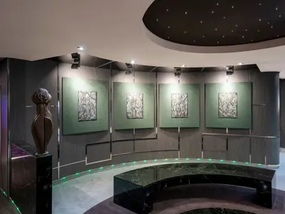 Elegante Kunstgalerie an Bord der MSC Splendida mit moderner Holzskulptur, vier gerahmten Metallbildern an der Wand und einem geschwungenen Marmortresen mit grüner LED-Beleuchtung.