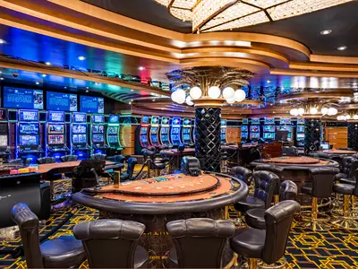 Eine Weitwinkelaufnahme des eleganten Royal Palm Casinos an Bord der MSC Splendida, beleuchtet mit blauen Lichtern und zahlreichen Slot-Maschinen und Spieltischen, bereit für Gäste.