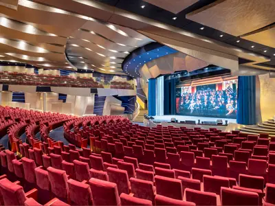 Blick in das 'The Strand Theatre' an Bord der MSC Splendida mit unzähligen roten Samtsitzen. Eine große Bühne mit LED-Bildschirm und eine elegante Wendeltreppe sind zu sehen.