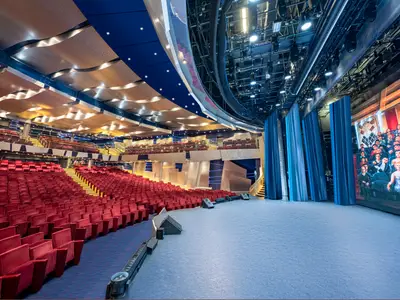 Theater an Bord der MSC Splendida: Hunderte leere rote Samtsitze, Bühne mit blauen Vorhängen und grosser LED-Wand, moderne Deckenbeleuchtung.