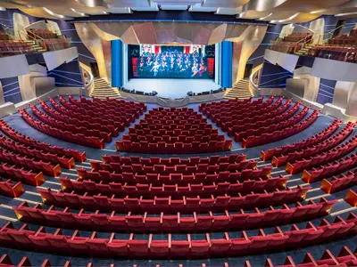 The Strand Theater der MSC Splendida, von oben. Leere rote Sitze, moderne Architektur, blaue Lichter. Große LED-Bühne mit Bild. Geschwungene Treppen zu den Rängen.