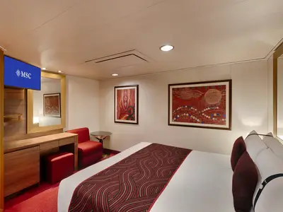 Eine moderne Innenkabine an Bord der MSC Splendida mit einem großen Doppelbett, einer roten Sitzgruppe und einem Schminktisch mit TV. Zwei Kunstwerke hängen an der Wand.