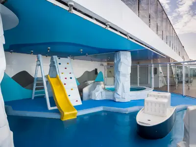 Der farbenfrohe Kinderbereich 'Il Polo Nord' auf der MSC Splendida zeigt eine gelbe Rutsche, Kletterwand und eisbergfoermige Dekorationen um blaue Planschbecken. Ein spielerischer Ort fuer Kinder.