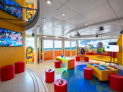 Ein farbenfroher Lego® Club an Bord der MSC Splendida mit Mario Kart-Bildschirmen, Legotischen und roten Hockern. Lebhafter Spielbereich.