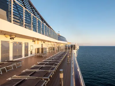 Blick auf das leere Sonnendeck der MSC Splendida mit zahlreichen gestapelten Sonnenliegen und dem tiefblauen Meer. Das warme Sonnenlicht beleuchtet die Bordwand und das Deck.