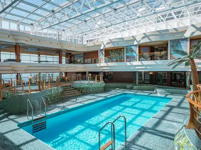 Blick auf den grossen Innenpool L'Equatore der MSC Splendida. Ein Oberlichtdach überspannt den Poolbereich mit Whirlpools und Palmen.