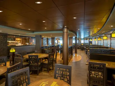 Asiatisch inspiriertes Restaurant an Bord der MSC Splendida. Dunkle Holzeinrichtung mit Tischen, Stühlen, Sitzbänken und einer Bar. Warme Beleuchtung.