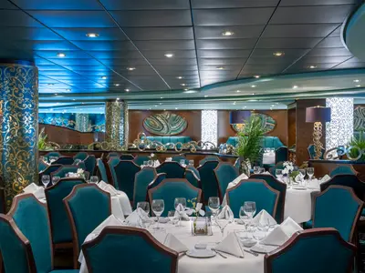 Innenansicht des eleganten Villa Verde Restaurants an Bord der MSC Splendida mit zahlreichen gedeckten Tischen, teal-farbenen Stühlen und goldverzierten Säulen.