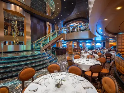 Elegantes Restaurant auf der MSC Splendida, mit gedeckten Tischen, beleuchteter Marmortreppe und Meerblick durch Bullaugen.