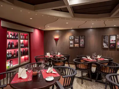 Ein stilvolles Spezialitätenrestaurant Butcher's Cut an Bord der MSC Splendida mit dunklen Holzwänden, roten Akzenten und elegant gedeckten Tischen. Eine beleuchtete Weinregalwand ist sichtbar.