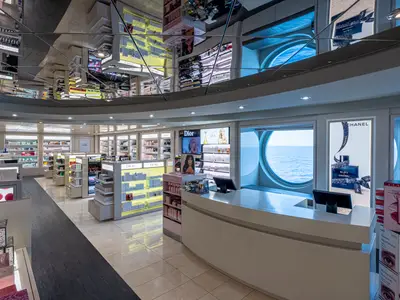 Heller Kosmetikshop an Bord der MSC Splendida. Elegante Auslagen mit Parfüms und Kosmetik. Runde Bullaugen bieten Meerblick. Eine reflektierende Decke spiegelt den Raum. Ohne Personen.