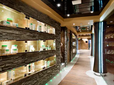 Eleganter Korridor der MSC Splendida. Steinwände mit beleuchteten Vitrinen voller Wellnessprodukte. Holz-Stein-Boden mit grünen LEDs. Glänzende Säulen. Modernes Spa-Design.