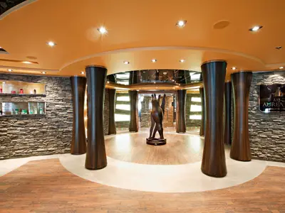 Eingangsbereich des MSC Aurea Spa an Bord der MSC Splendida. Eine Holzskulptur steht im Zentrum, umgeben von geschwungenen Holzsäulen, Steinwänden und einem leuchtenden Deckenbereich. Produkte sind in Wandnischen ausgestellt.