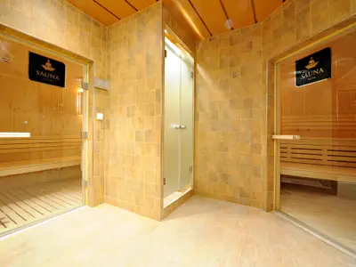 Der helle Spa-Bereich an Bord der MSC Splendida präsentiert zwei Holzsaunen, ‘Vetiver’ und ‘Musk’, getrennt durch eine Milchglas-Duschkabine. Beige Fliesen bedecken die Wände.