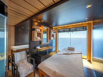 Ein heller, luxuriöser Behandlungsraum im MSC Aurea Spa an Bord der MSC Splendida mit zwei Massageliegen und einem Waschbecken, umgeben von großen Fenstern mit weitem Meerblick.