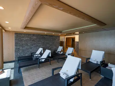 Entspannungsbereich im MSC Aurea Spa an Bord der MSC Splendida. Dunkle Lounge-Liegen mit weißen Handtüchern. Eine Steinwand und helle Holzwände. Links ein großes Fenster mit Meerblick.