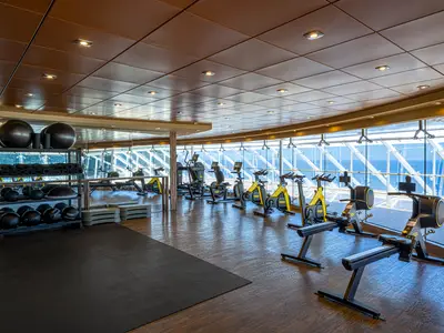 Ein geräumiges Fitnessstudio an Bord der MSC Splendida, ausgestattet mit Rudergeräten, Fahrrädern und Hanteln. Grosse Fenster bieten einen weiten Blick auf das offene Meer.