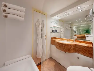 Ein luxuriöses Badezimmer in einer Suite an Bord der MSC Splendida, ausgestattet mit einem orangefarbenen Marmorwaschtisch, einem grossen Spiegel, weissen Bademänteln und bestickten Handtüchern.