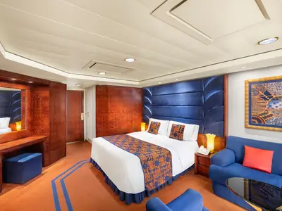 Geräumige Grand Suite der MSC Splendida mit Doppelbett, blauem Sofa, Schminktisch und Holzinterieur. Helle Decke und orangefarbener Teppich.