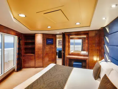 Ein luxuriöses Schlafzimmer in einer Grand Suite Aurea an Bord der MSC Splendida. Zu sehen sind ein großes Bett, dunkle Holzvertäfelungen, eine Sitzecke und ein Balkon mit Meerblick.