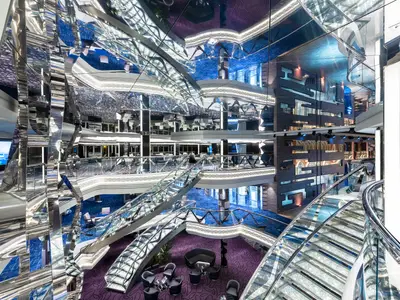 Blick in das luxuriöse, mehrstöckige Infinity Atrium der MSC Virtuosa. Glitzernde Swarovski-Kristalltreppen und spiegelnde Wände prägen das moderne Design mit blauen und lila Teppichen. Ohne Personen.