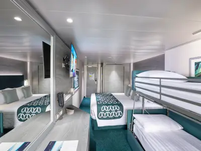 Geräumige Familienkabine der MSC Virtuosa mit grossem Doppelbett, einem Etagenbett und modernem Dekor in Blau- und Grautönen. Ein Spiegeltisch und Fernseher sind ebenfalls zu sehen.