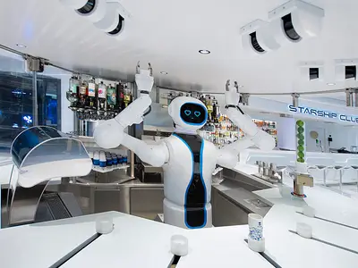 Im MSC Starship Club an Bord der MSC Virtuosa steht der futuristische Roboter-Barkeeper Rob. Er hat vier Arme und zwei blaue Herz-Augen. Im Hintergrund Flaschen und ein beleuchteter Tresen.