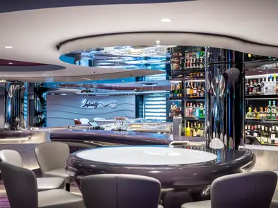 Die moderne Infinity Bar an Bord der MSC Virtuosa. Geschwungene Theke, reflektierende Oberflächen und beleuchtete Flaschenregale voller Getränke. Das Logo "Infinity BAR" ist an der Wand sichtbar.