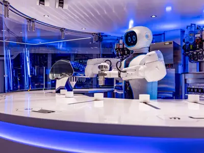 Der futuristische MSC Starship Club an Bord der MSC Virtuosa. Ein weißer Roboter-Barkeeper mixt Drinks am Tresen. Blaue LED-Beleuchtung akzentuiert den Barbereich mit Flaschen und Gläsern.