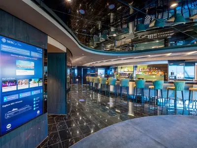 Moderne Bar mit Barhockern und schwarzer Marmor-Oberfläche an Bord der MSC Virtuosa. Links ein großer interaktiver Touchscreen. Die spiegelnde Decke reflektiert das Interieur.