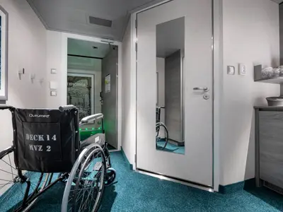 Blick in eine barrierefreie Kabine an Bord der MSC Virtuosa. Im Vordergrund ein Rollstuhl. Die helle, modern eingerichtete Kabine zeigt eine breite Tür und einen Schrankbereich.