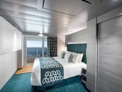Helle, moderne Balkonkabine an Bord der MSC Virtuosa mit einem Doppelbett, blauer Teppich, Holzdetails und Zugang zu einem privaten Balkon mit Meerblick.