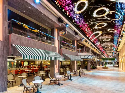 Eine Aufnahme der beleuchteten Galleria Virtuosa an Bord der MSC Virtuosa, einer Promenade mit Geschäften, Cafés und einem farbenfrohen LED-Himmel.