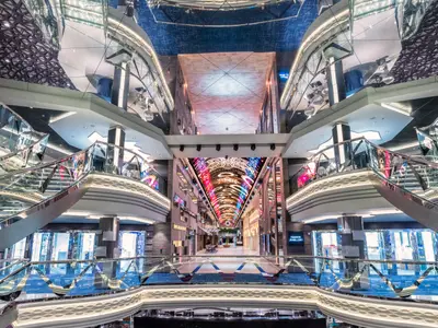 Weitwinkelaufnahme der mehrstöckigen Galleria Virtuosa an Bord der MSC Virtuosa. Eine lange Promenade mit Geschäften, gläsernen Treppen und einem spektakulären LED-Himmel erstreckt sich durch das Schiff.