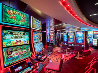 MSC Virtuosa Casino: Reihen modernster Spielautomaten leuchten hell. Rote und blaue Neonlichter erhellen den Raum mit gemustertem Teppich und Barhockern.