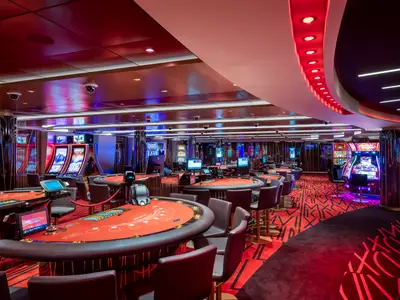 Das Red Gem Casino an Bord der MSC Virtuosa zeigt sich in modernem Design mit roten Spieltischen und zahlreichen leuchtenden Slotmaschinen, bereit fuer die Abendunterhaltung.