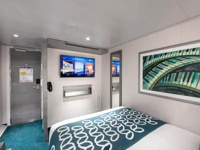 Moderne Innenkabine an Bord der MSC Virtuosa mit einem Bett, Flachbildfernseher, einer Tür und einem Spiegel. Ein Kunstwerk mit Klaviertasten schmückt die Wand. Ohne Personen.