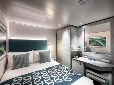 Blick in eine modern eingerichtete Innenkabine der MSC Virtuosa. Zu sehen sind ein gemachtes Doppelbett mit Kissen, ein Nachttisch mit Lampe, ein Schminktisch mit Spiegel und integriertem Schrank.