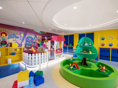 Farbenfroher LEGO Junior Club Spielbereich an Bord der MSC Virtuosa mit Wandmalereien, Spielstationen und LEGO Bausteinen. Keine Personen zu sehen.