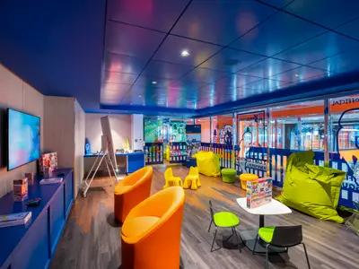 MSC Teens Lab an Bord der MSC Virtuosa. Ein lebhaftes Jugendzimmer mit Gaming-Bildschirmen, blauer Einrichtung, bunten Sitzen und Fenster zur Promenade.