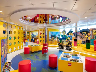 Ein farbenfroher LEGO-Miniclub an Bord der MSC Virtuosa. Grosse LEGO-Figuren, Bausteine und Spielbereiche sind in dem lebhaften Raum zu sehen. Der Boden ist mit einer Weltkarte gestaltet.