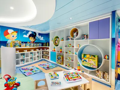 Der helle und farbenfrohe Baby Club Chicco an Bord der MSC Virtuosa. Weiße Regale sind gefüllt mit Spielzeug, dazu bunte Wandmalereien und Kindermöbel.
