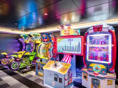 Ein lebhafter Spielhallenbereich an Bord der MSC Virtuosa mit bunten Arcade-Automaten wie Rennmotorrädern, Glücksrädern und einem Sonic-Spiel. Die Geräte leuchten in verschiedenen Farben und schaffen eine spielerische Atmosphäre.