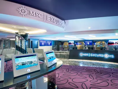 Interaktiver MSC Excursions Bereich an Bord der MSC Virtuosa mit digitalen Info-Bildschirmen und Empfangstheke.