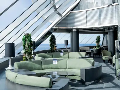 Moderne Lounge an Bord der MSC Virtuosa. Große Glasfenster bieten weiten Meerblick. Elegante grüne Rundsofas, Tische und Pflanzen schmücken den hellen Raum.