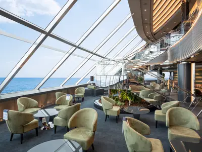 Elegante Top Sail Lounge an Bord der MSC Virtuosa. Die grossen Fenster bieten weiten Meerblick. Bequeme Sessel und eine geschwungene Treppe prägen den modernen Raum.
