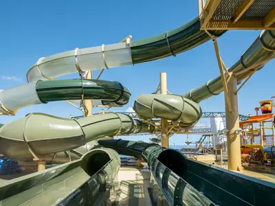 Der Savannah Aquapark auf der MSC Virtuosa. Grüne und transparente Wasserrutschen schlängeln sich über das obere Deck unter blauem Himmel. Ein spielerischer Ort für Familien und Wasserspaß.