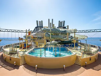 Blick auf den weitläufigen Savannah Aquapark an Bord der MSC Virtuosa mit mehreren Wasserrutschen, Seilgarten und Pools unter blauem Himmel. Ohne Personen.