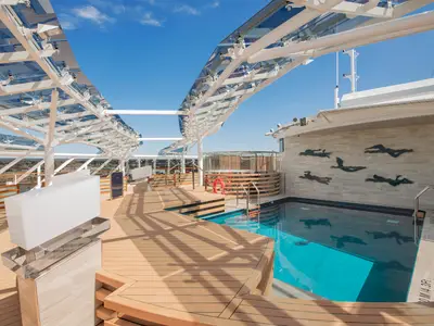 Blick auf den exklusiven Poolbereich des MSC Yacht Club an Bord der MSC Virtuosa. Ein hellblauer Pool, ein Whirlpool und ein stilvolles Glasdach sind unter blauem Himmel zu sehen.